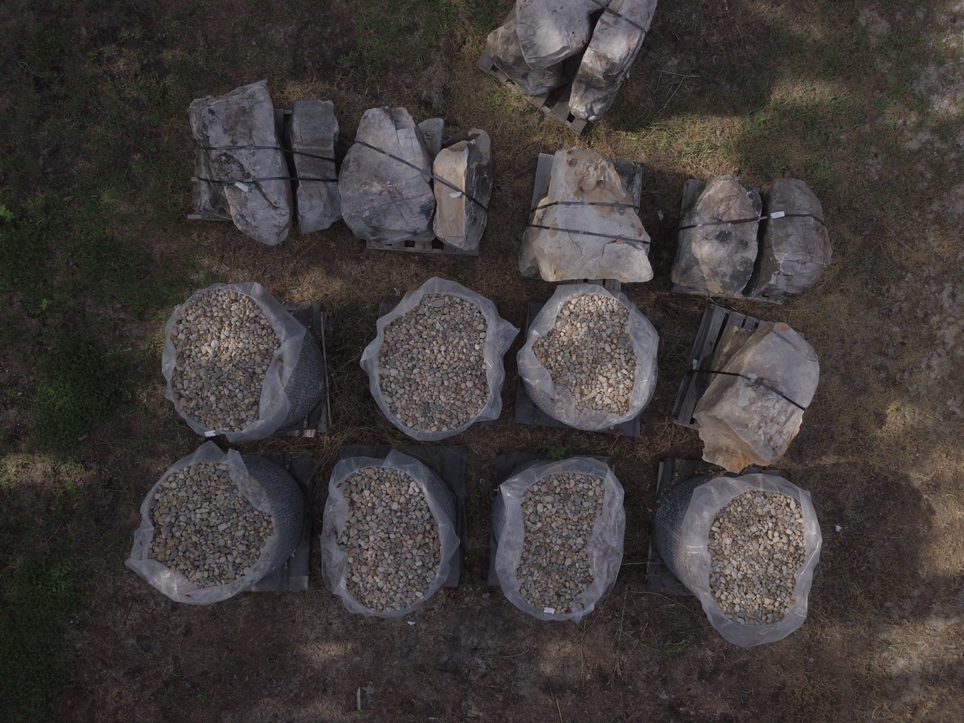 Pallets of boulders and bulk bags of river rock in the yard